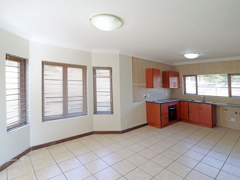 Spacious open-plan kitchen and living area featuring tiled floors, built-in cabinetry, integrated oven, and large windows with venetian blinds.