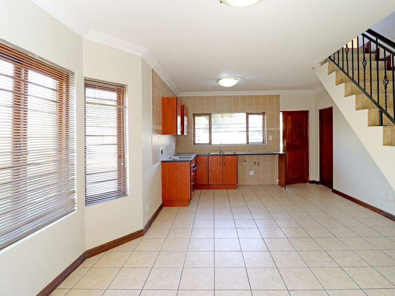 An open-plan kitchen and living area featuring tiled floors, wooden cabinetry, and a staircase leading to the upper level.