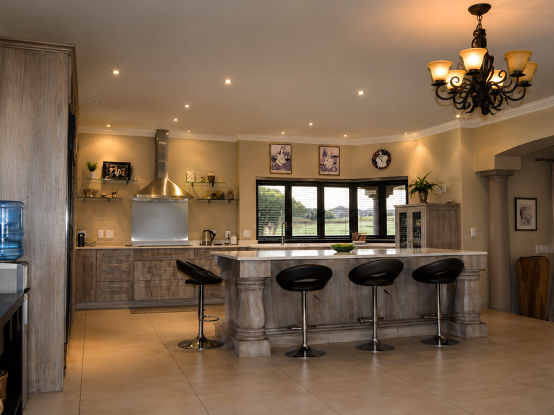 Spacious kitchen featuring a large central island with stone countertops, custom cabinetry, stainless steel extractor fan, and elegant lighting, overlooking a scenic garden view.