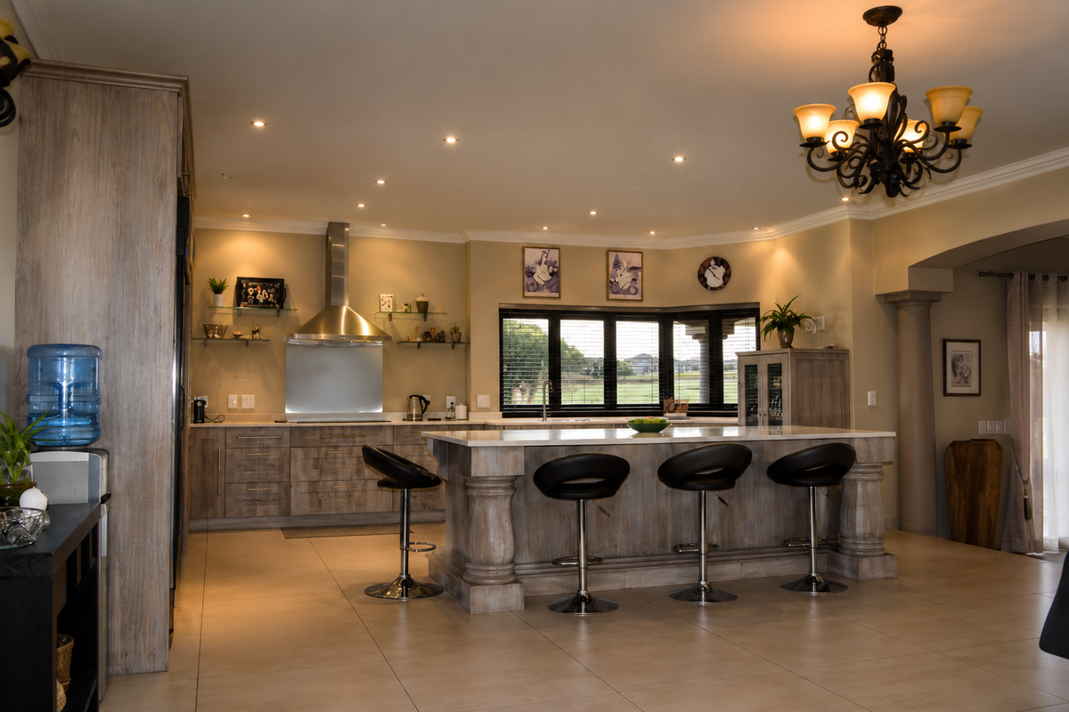 Spacious kitchen featuring a large central island with stone countertops, custom cabinetry, stainless steel extractor fan, and elegant lighting, overlooking a scenic garden view.