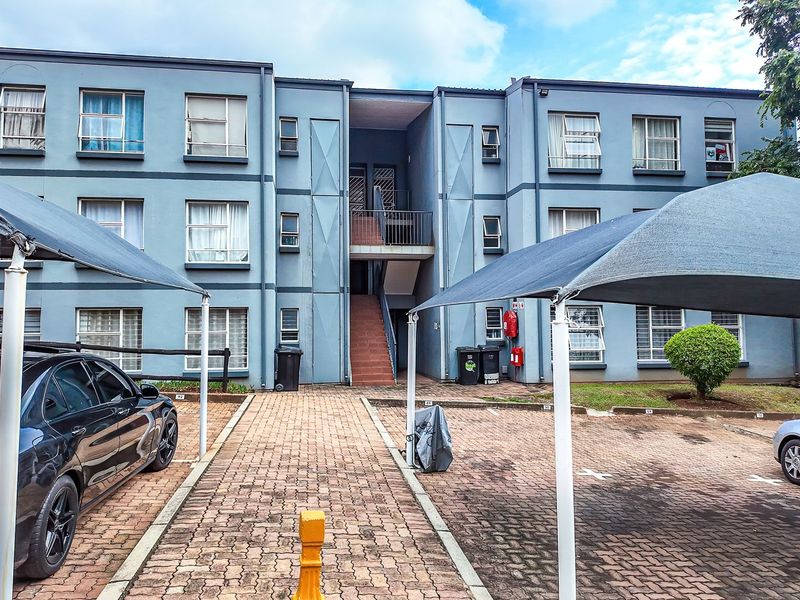 Front view of a multi-story apartment complex featuring paved parking areas with shade cloth carports and central stairwell access.