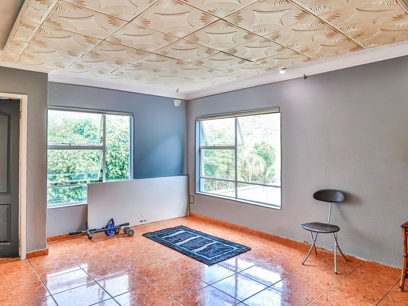 A spacious living area featuring tiled flooring, decorative ceiling tiles, and large windows providing natural light. The room is currently vacant and ready for renovation.