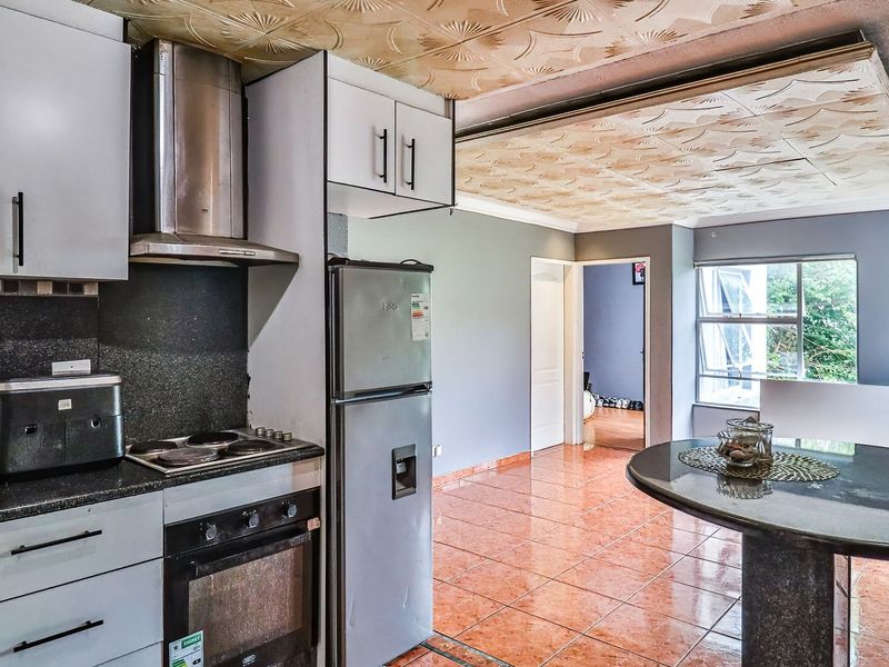 Open-plan kitchen and living area featuring granite countertops, built-in appliances, tiled flooring, and decorative ceiling tiles, offering a functional layout with potential for modernization.