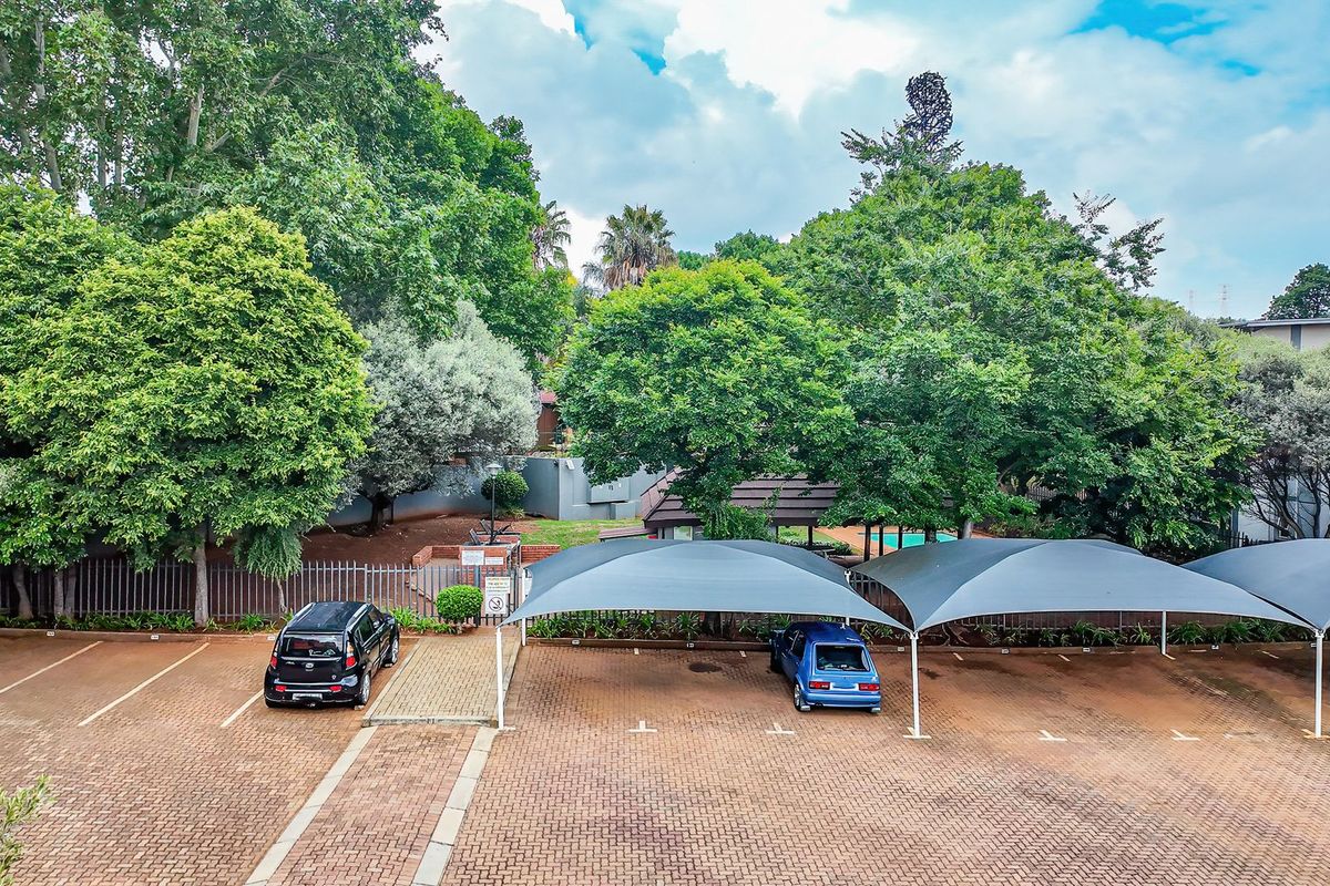 An elevated view of the apartment complex parking area featuring paved bays, shade cloth carports, and established surrounding greenery.