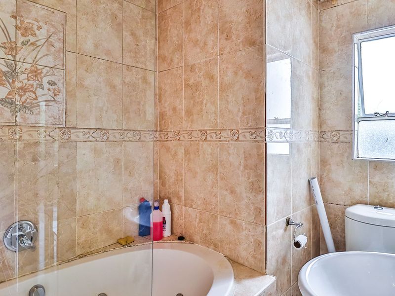 A functional bathroom featuring a built-in bathtub with a glass screen, pedestal basin, and neutral ceramic wall tiling with decorative accents.
