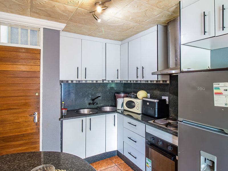 Compact kitchen featuring granite countertops, built-in cabinetry, integrated oven and hob, and a double bowl sink.
