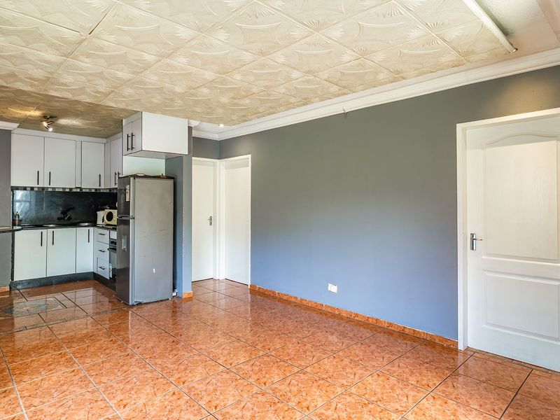 Open plan living and kitchen area featuring tiled flooring, built-in cabinetry, and a breakfast bar, offering a functional layout ready for modernization.