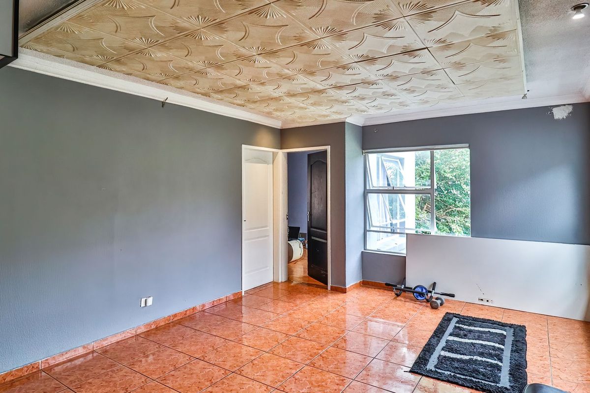 Spacious living area featuring tiled flooring, decorative ceiling panels, and large windows allowing natural light, ready for a modern update.