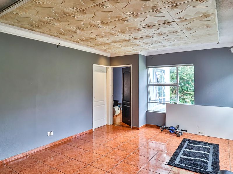 Spacious living area featuring tiled flooring, decorative ceiling panels, and large windows allowing natural light, ready for a modern update.