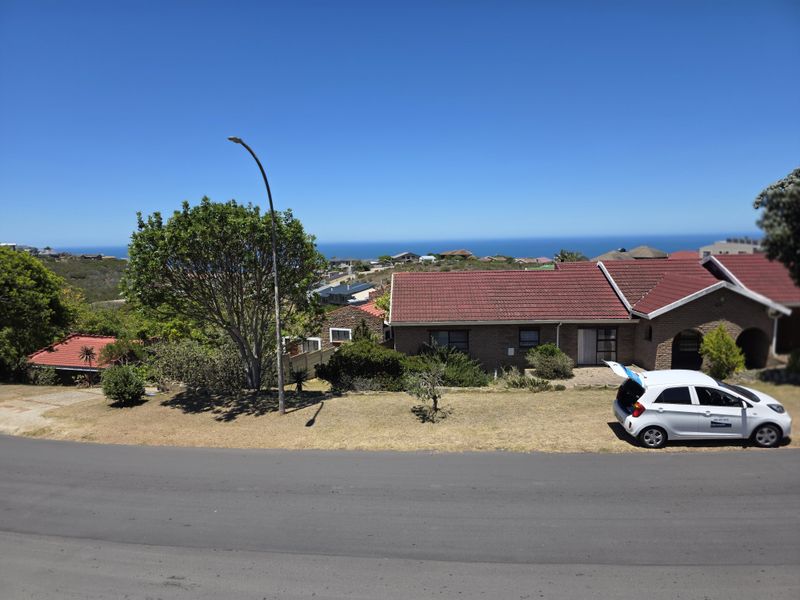 A street-level view of a residential property featuring a brick facade, tiled roof, and distant ocean views in a coastal neighborhood.
