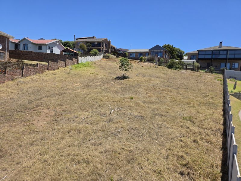 A vacant residential plot featuring a gentle slope, enclosed by boundary walls and fencing, situated within an established neighbourhood.