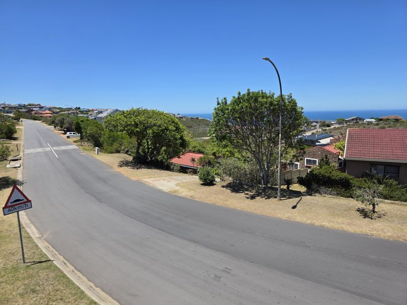 A street view showing the residential road, surrounding neighborhood, and distant ocean views in a coastal setting.