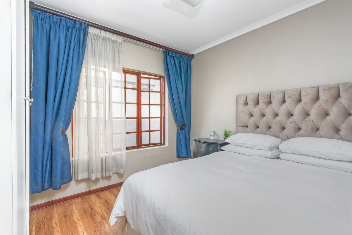 A well-maintained bedroom featuring laminate flooring and a timber-framed window with curtain fixtures.