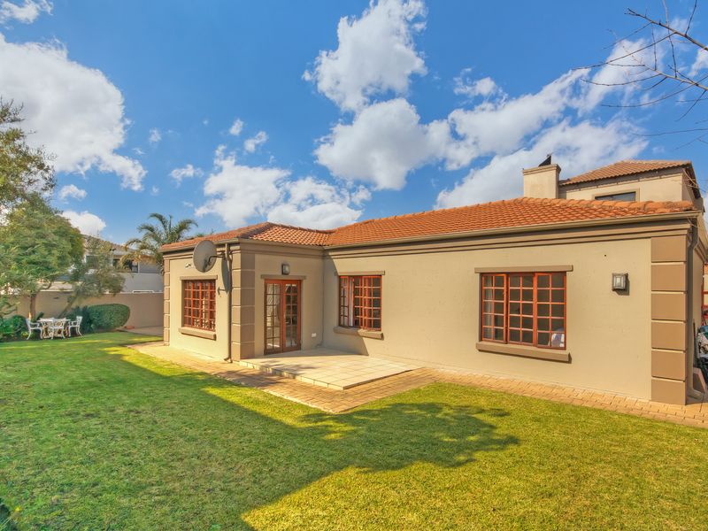Rear view of the property featuring a paved patio area, well-maintained lawn, and classic timber-framed windows and doors under a terracotta tiled roof.