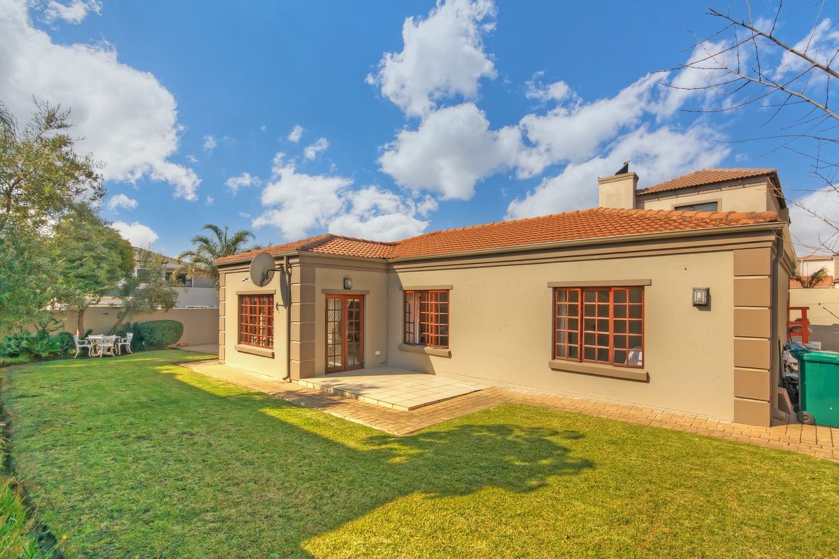 Rear view of the property featuring a paved patio area, well-maintained lawn, and classic timber-framed windows and doors under a terracotta tiled roof.