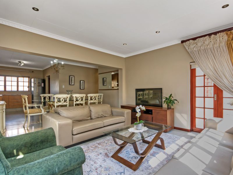 Open-plan living and dining area featuring tiled floors, recessed lighting, decorative cornices, and a timber-framed glass door leading to the exterior.