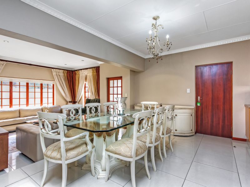 Spacious open-plan living and dining area featuring tiled flooring, crown molding, and a classic chandelier, seamlessly connecting to the kitchen space.