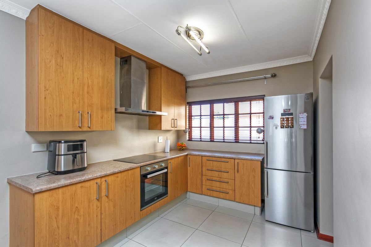 A functional kitchen featuring wood-look cabinetry, laminate countertops, built-in oven, electric hob, stainless steel extractor fan, and tiled flooring.