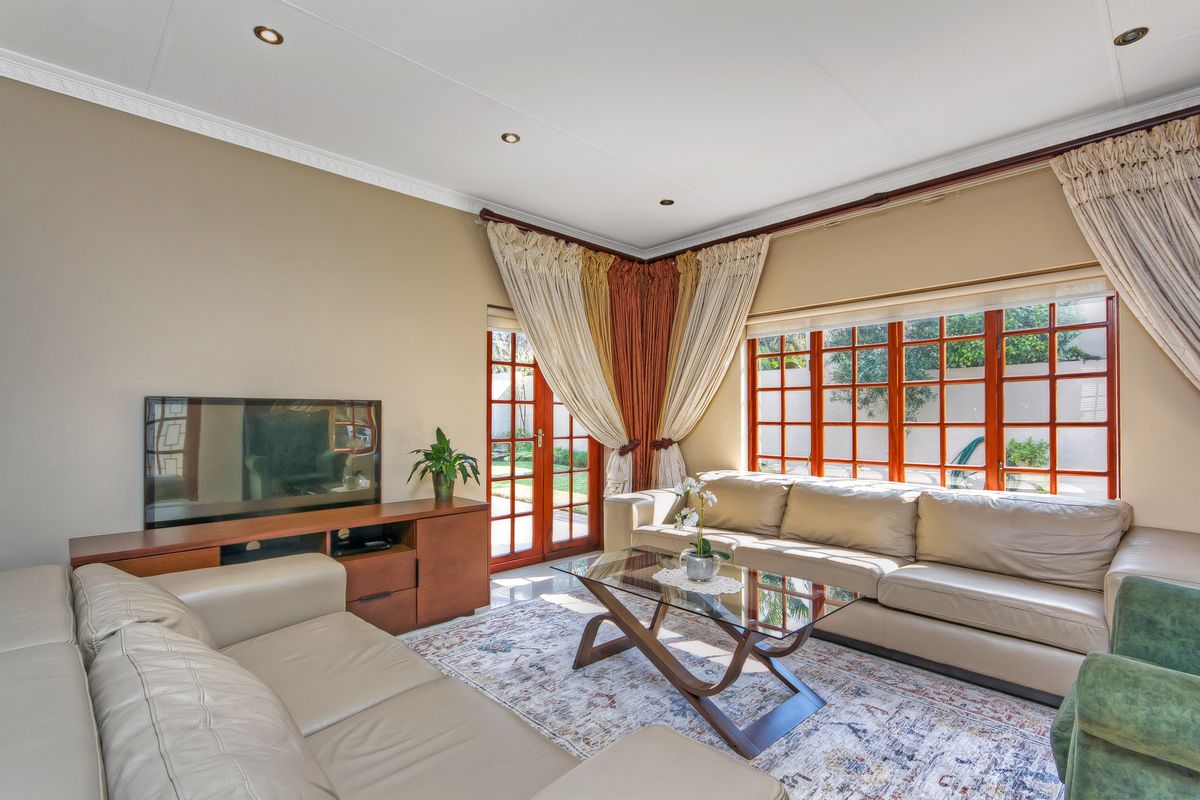A bright and comfortable living room featuring tiled flooring, recessed downlights, and large timber-framed windows that provide ample natural light and garden access.