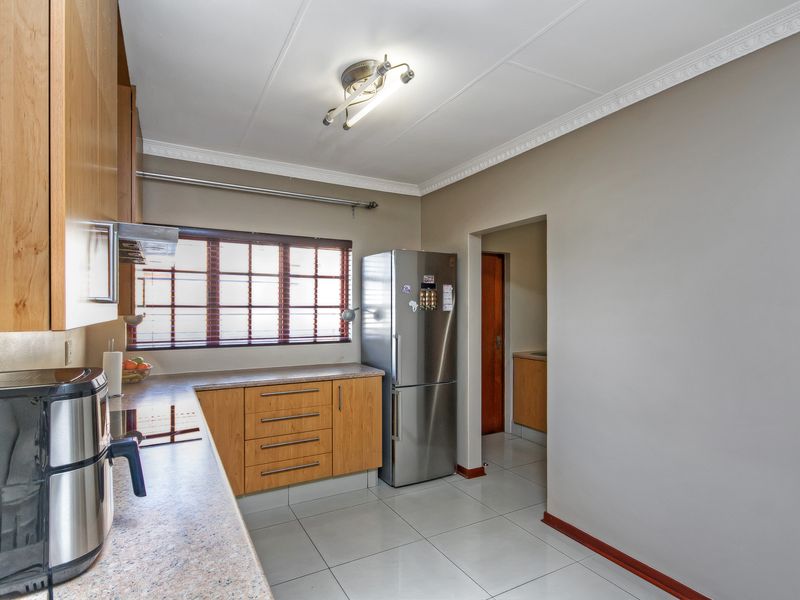 A functional kitchen featuring light wood cabinetry, laminate countertops, ceramic floor tiles, and a ceiling-mounted light fixture, with an adjacent scullery area.