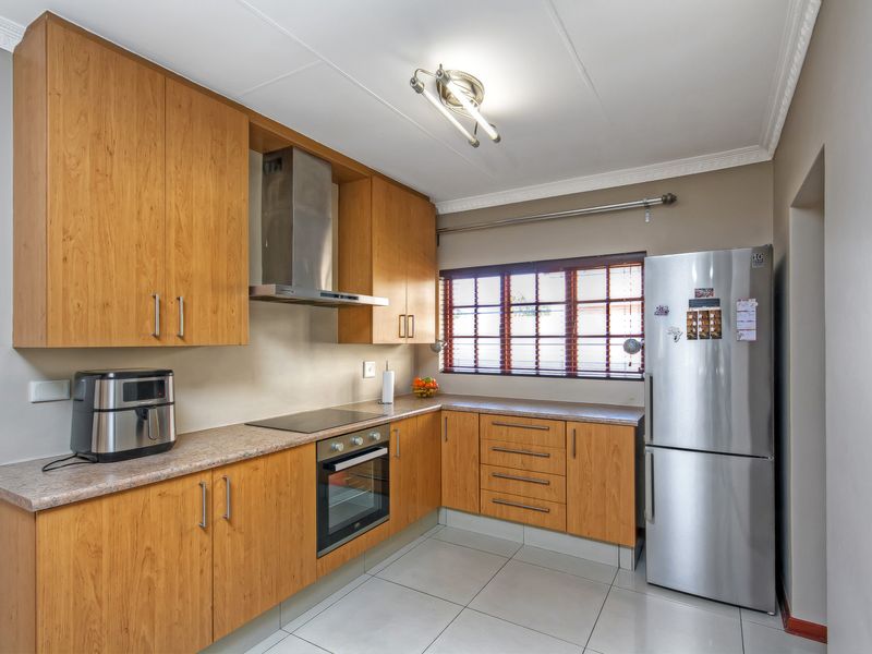 A functional kitchen featuring wood-look cabinetry, laminate countertops, built-in oven, electric hob, stainless steel extractor fan, and tiled flooring.