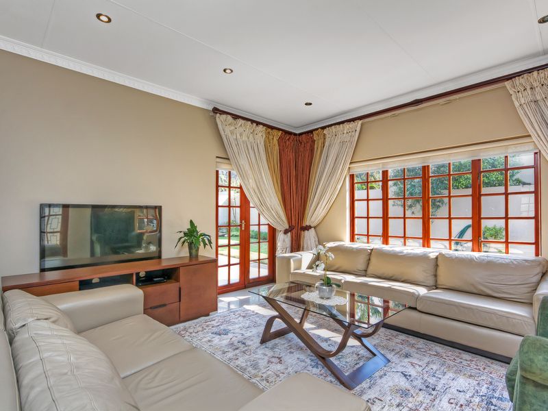 A bright and comfortable living room featuring tiled flooring, recessed downlights, and large timber-framed windows that provide ample natural light and garden access.