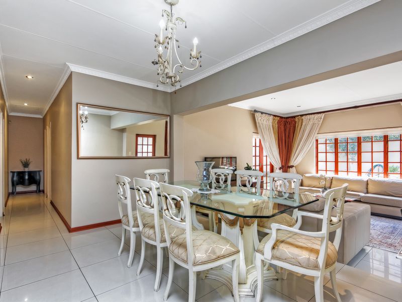 Spacious open-plan dining and living area featuring tiled flooring, crown molding, and abundant natural light through large windows.