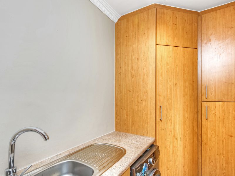 A functional laundry area featuring built-in wooden cabinetry, a laminate countertop, and a stainless steel sink with a modern faucet.
