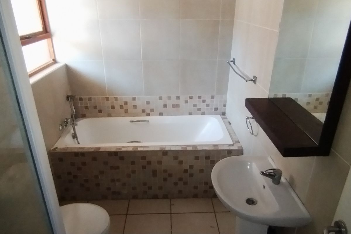 A functional bathroom featuring a built-in bathtub with mosaic tile surround, a pedestal basin, and a wall-mounted mirror.
