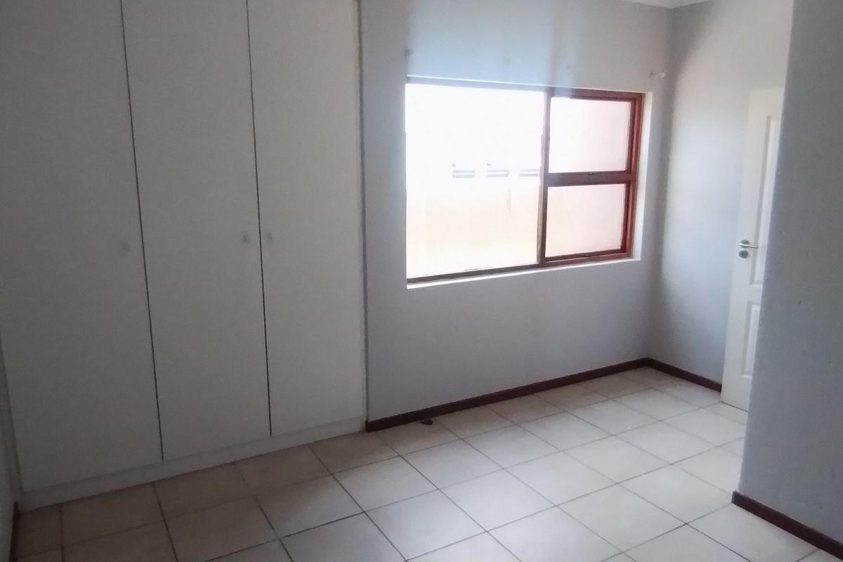 A bright, empty bedroom featuring built-in cupboards, tiled flooring, and a window providing natural light.