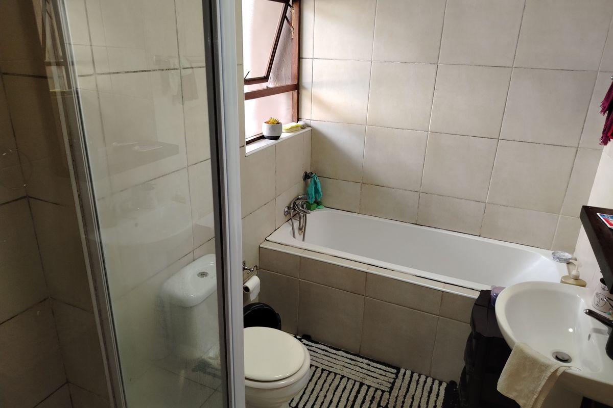 A functional bathroom featuring a built-in bathtub, separate glass-enclosed shower, pedestal basin, and toilet with neutral wall tiling.