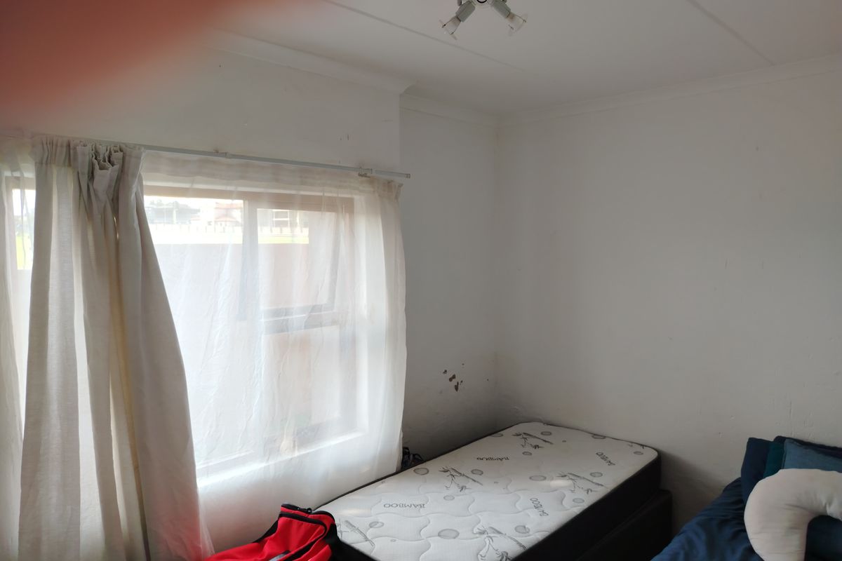 A bedroom featuring a window with curtain tracks and a ceiling-mounted light fixture, showing signs of wear on the wall surfaces.