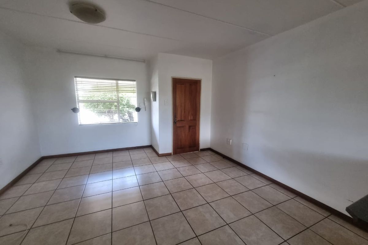 An empty living room featuring neutral floor tiles, a wooden door, and a window with fitted blinds, offering a blank canvas for personalization.
