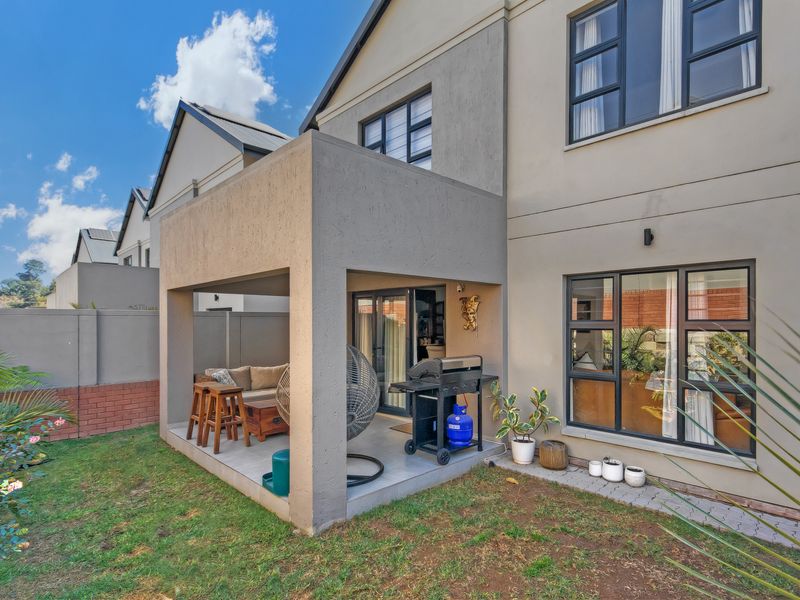 Rear view of the townhouse featuring a covered patio with tiled flooring, aluminium window frames, and a private garden area.
