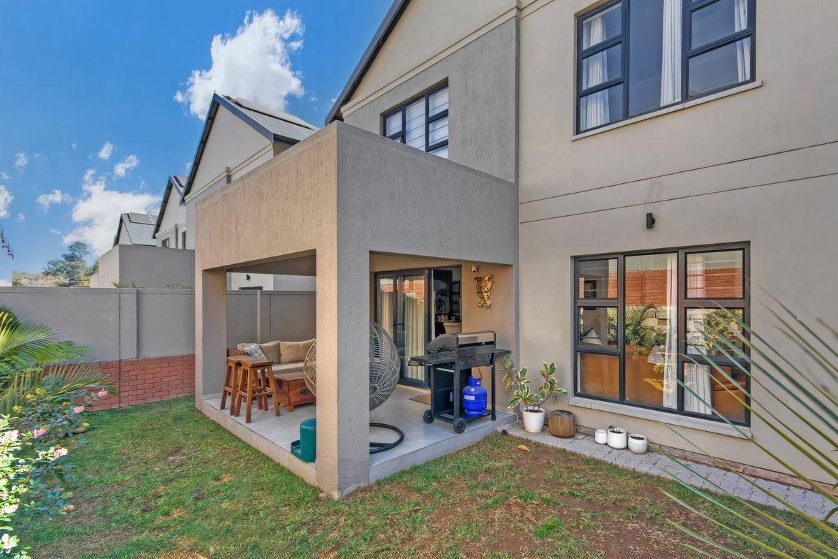 Rear view of the townhouse featuring a covered patio with tiled flooring, aluminium window frames, and a private garden area.