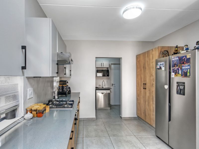 Modern kitchen featuring stone countertops, gas hob, extractor fan, and ample built-in cabinetry, with a convenient walk-through scullery area.