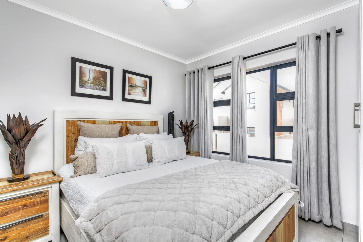 A well-maintained bedroom featuring neutral walls, tiled flooring, and large aluminium-framed windows with integrated curtain tracks.