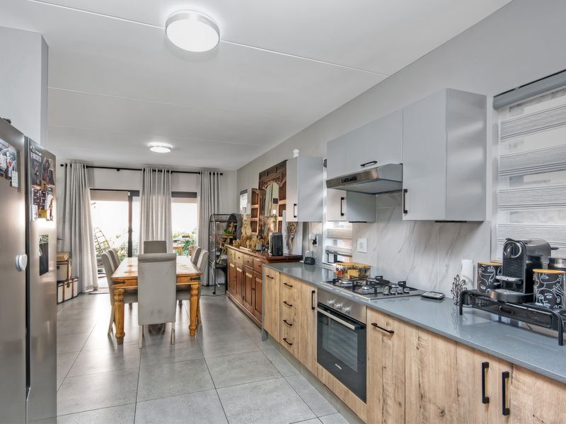 Modern open-plan kitchen and dining area featuring contemporary cabinetry, stone countertops, integrated appliances, and direct access to the patio through sliding glass doors.