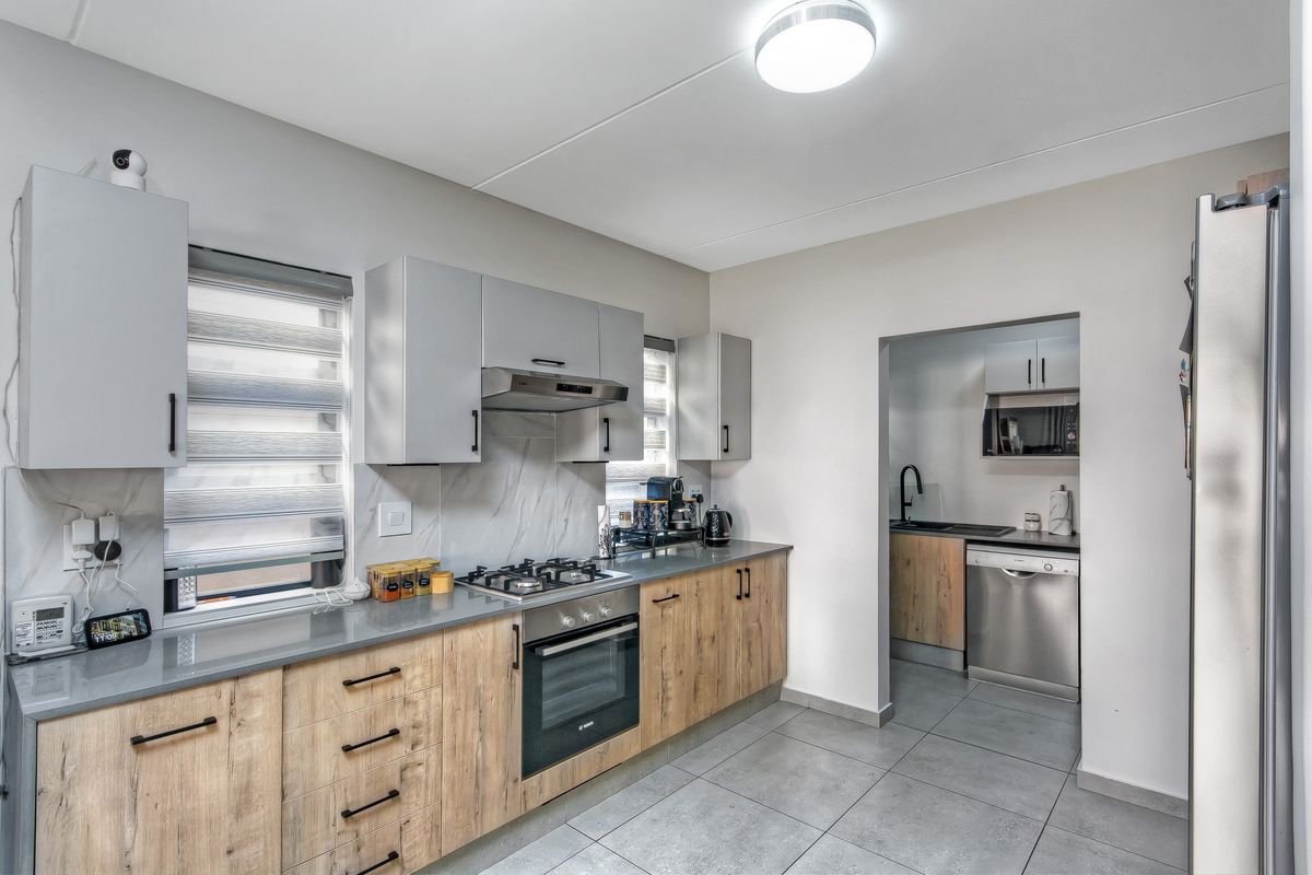 Modern kitchen featuring wood-grain cabinetry, stone countertops, gas hob, built-in oven, and an adjoining scullery area with additional sink and dishwasher space.