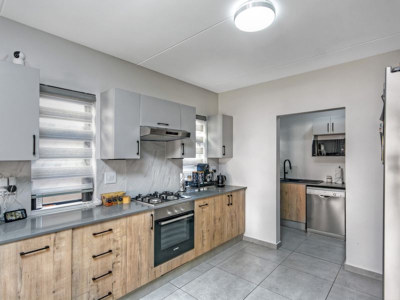 Modern kitchen featuring wood-grain cabinetry, stone countertops, gas hob, built-in oven, and an adjoining scullery area with additional sink and dishwasher space.