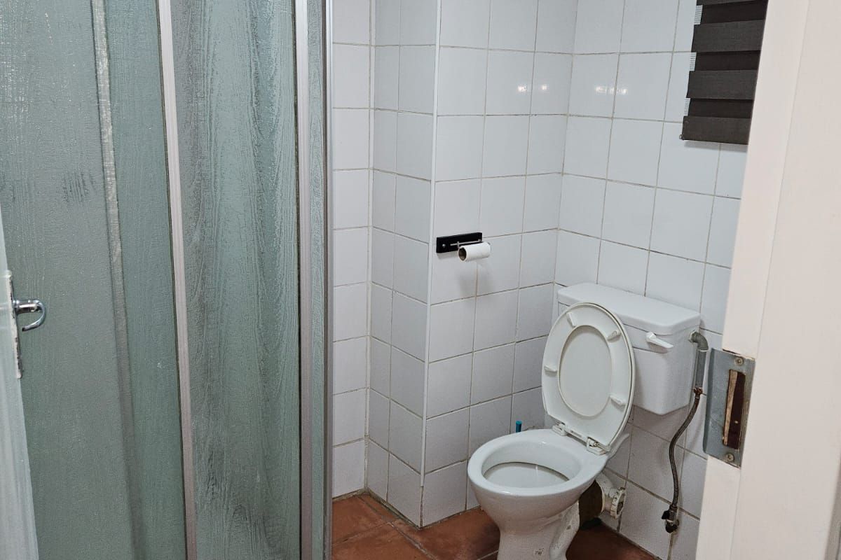 A compact bathroom featuring a shower enclosure, toilet, and tiled finishes. The space is functional but would benefit from modern updates.