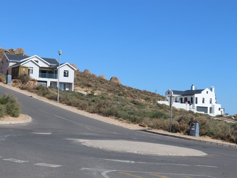 A street view showing the asphalt road, kerbing, and surrounding residential properties in a hillside estate setting.