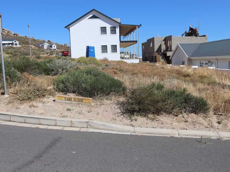 A street-level view of a vacant residential plot located on Yano Close, featuring natural vegetation and surrounding residential development.