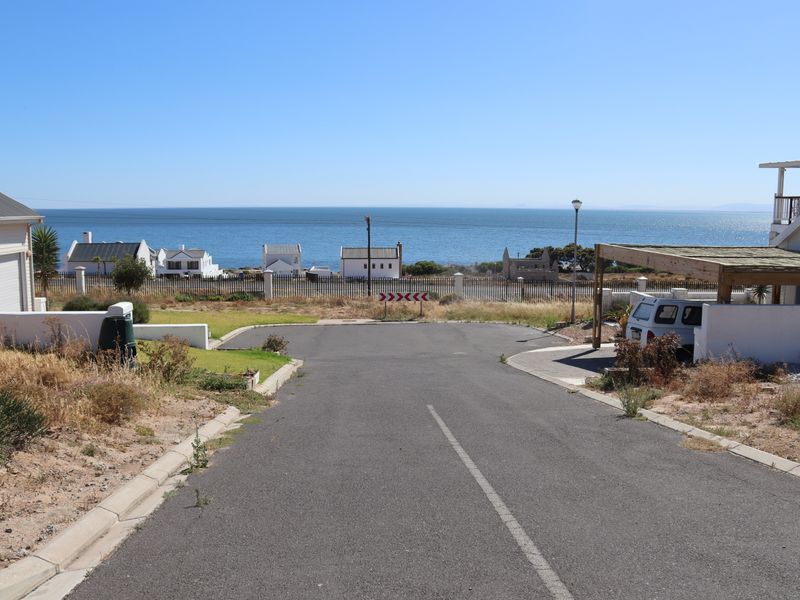 A street-level view of a residential road leading towards a coastal landscape with ocean views and surrounding properties.