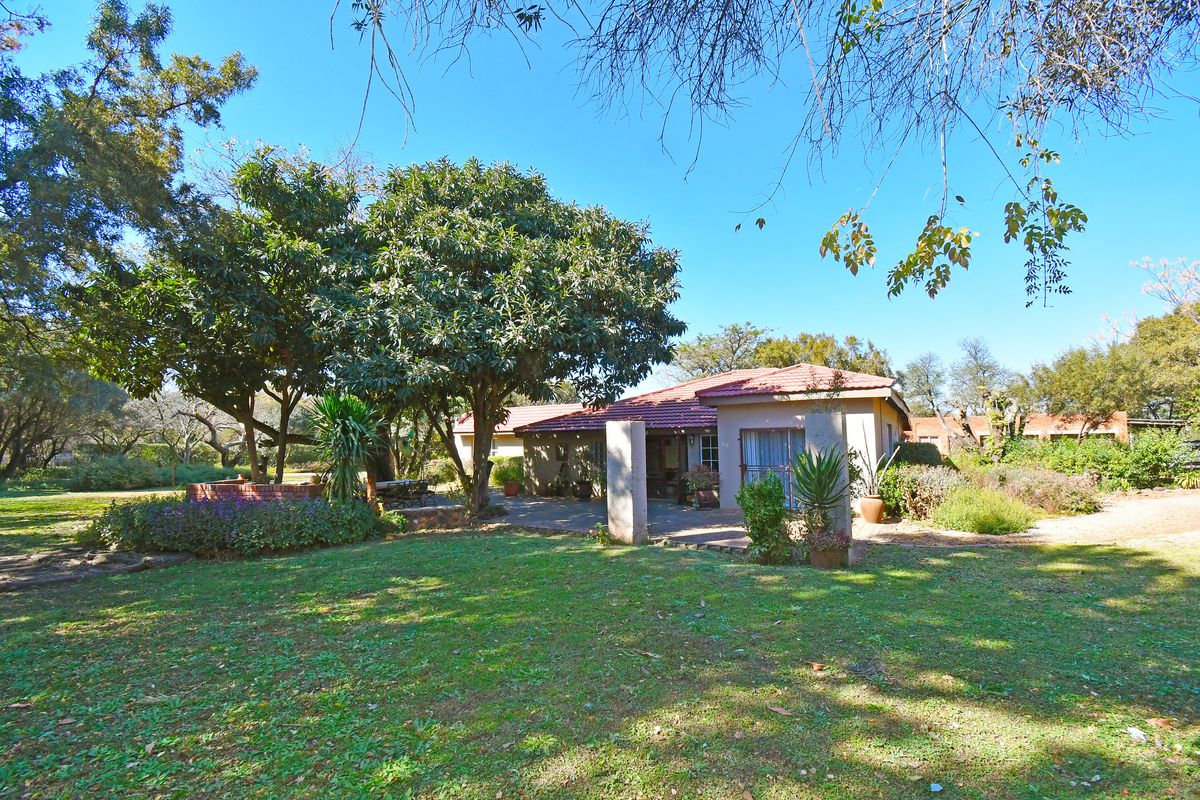 Rear view of the farm residence featuring a covered patio, established garden, and mature trees.