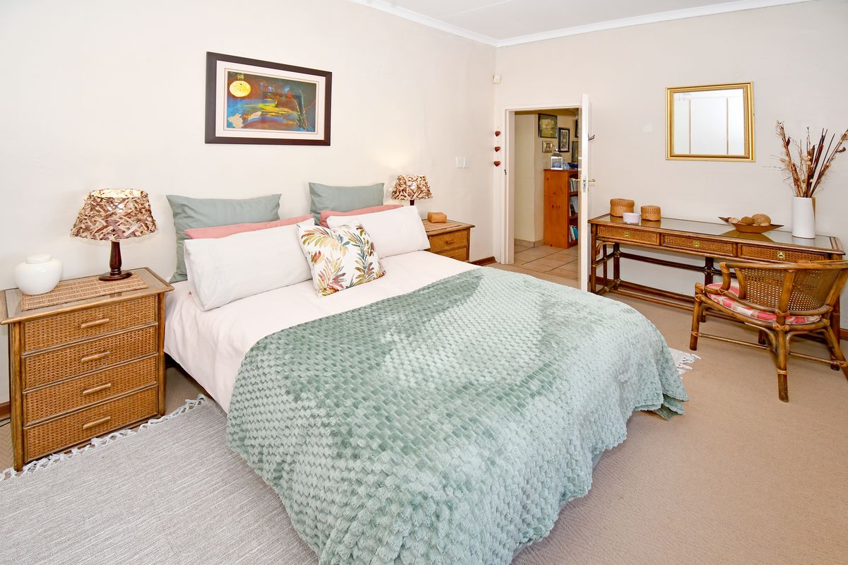 A well-lit bedroom featuring neutral wall tones, carpeted flooring, and a doorway leading to an adjacent room.