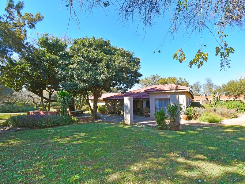 Rear view of the farm residence featuring a covered patio, established garden, and mature trees.