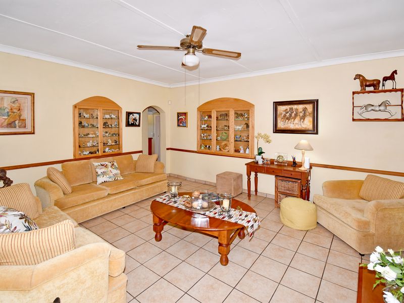 Spacious living room featuring ceramic tile flooring, a ceiling fan, and two built-in arched display cabinets with wooden frames.
