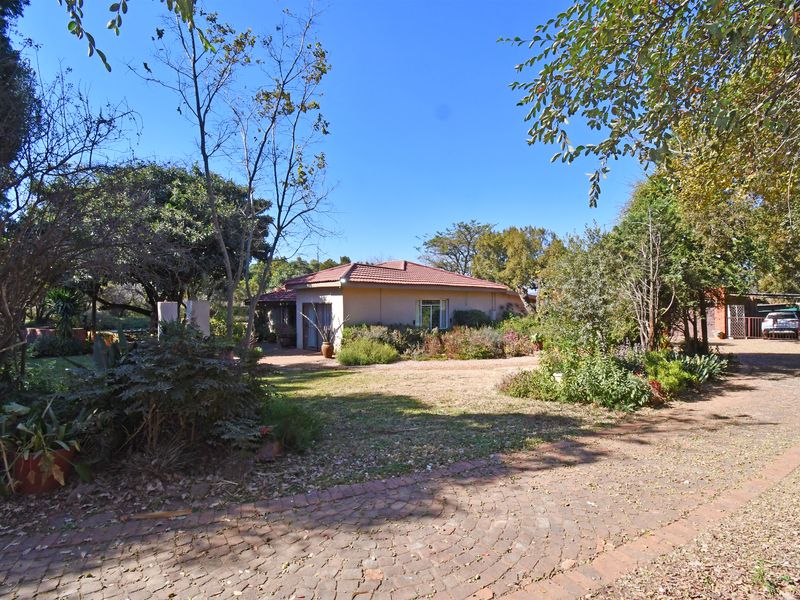 A view of the rear exterior of the farm property, featuring a brick paved driveway, established garden, and a covered patio area.