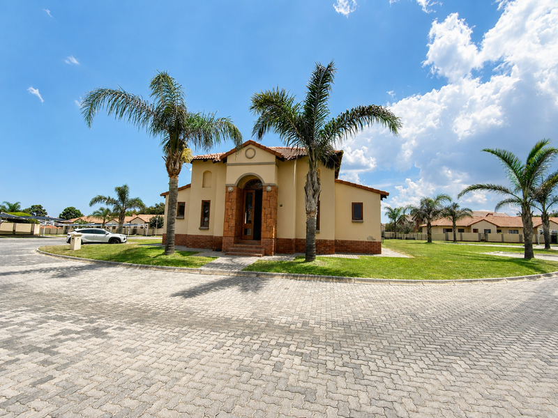 Front elevation of a residential apartment building featuring a tiled roof, brick facade, arched entrance, and a paved driveway surrounded by landscaped lawns.